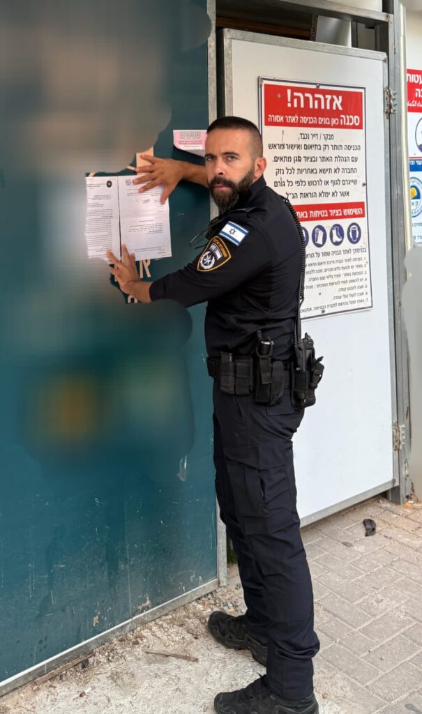צילום שוטר מצמיד את צו הסגירה על גדר אתר הבניה